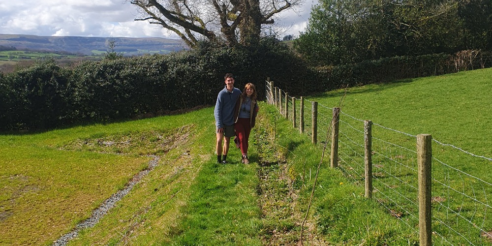 Offsetting Our Carbon Footprint: Young man and woman stood next to freshly planted row of shrubs